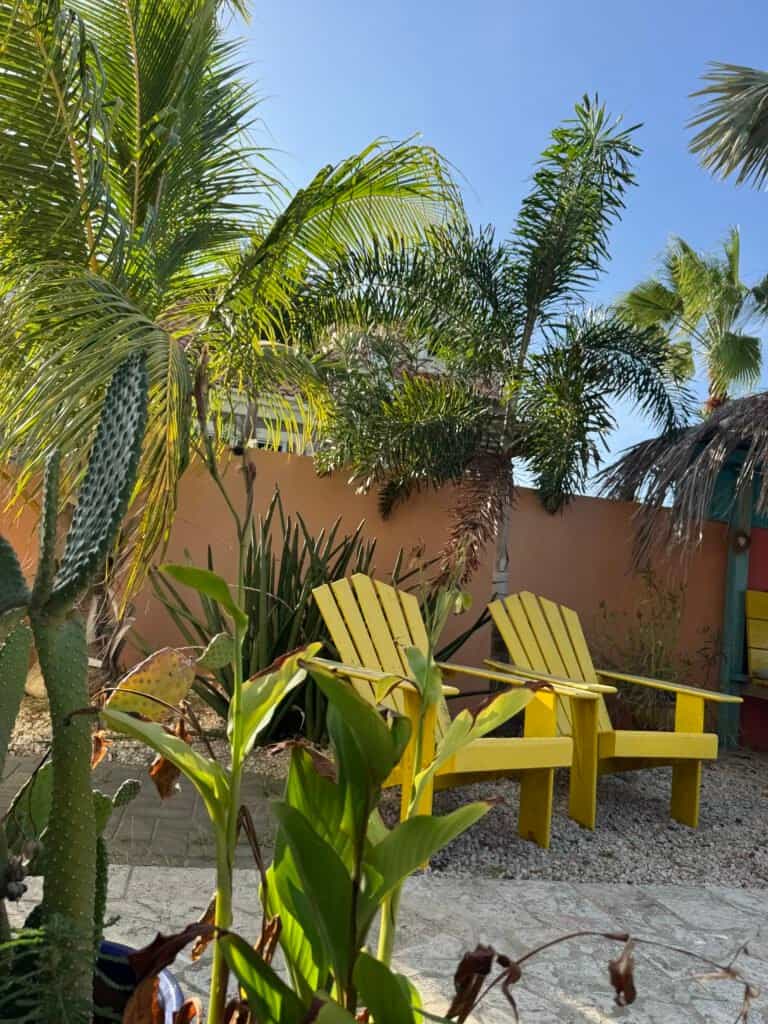 Zitplek met gele stoelen in de tropische tuin van Oasis Guesthouse Bonaire